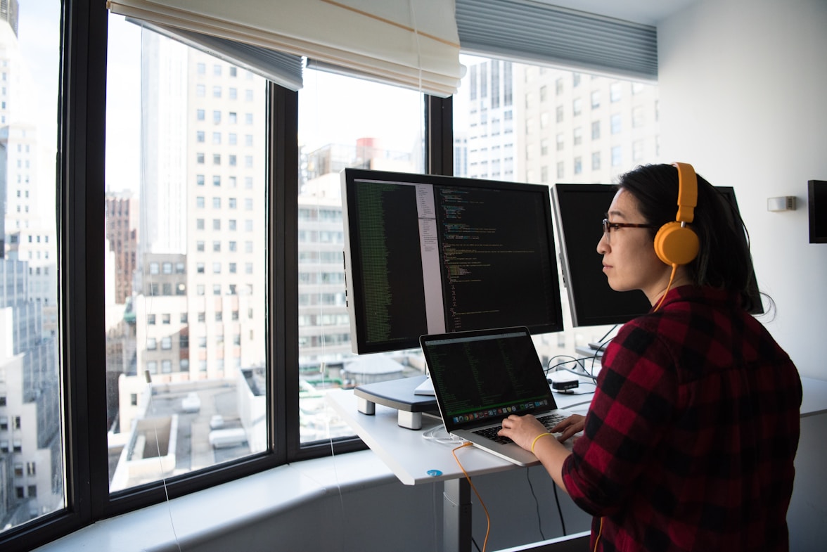 A person with headphones looking out of the window at their desk.